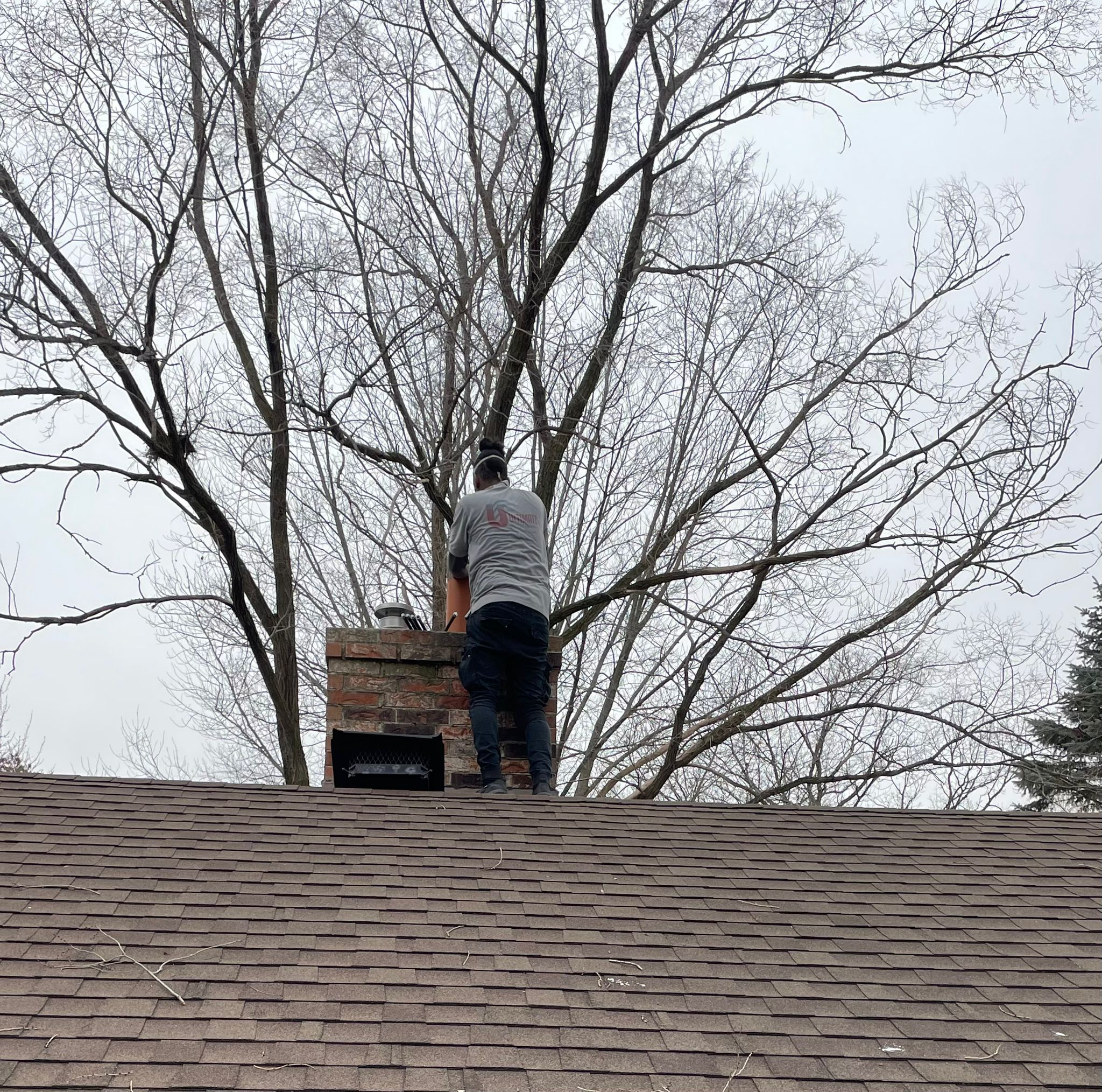 JB Chimney Services technicians applying breathable waterproof sealant to a stone-clad lakeside chimney in Minnetonka, MN.